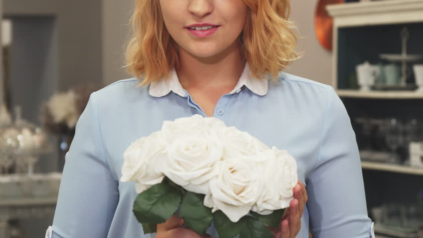 The girl is holding a bouquet of flowers in her hands. She takes them to her face and sniffs them. She wants to decorate her apartment with them. The girl came to the store