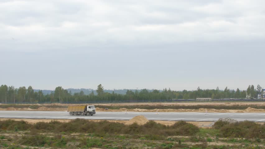 Big trucks rides on road. Truck is transporting material. Construction, concreting of airport runways, roads. Tippers, asphalt paver, roadroller, construction machinery works on runway construction