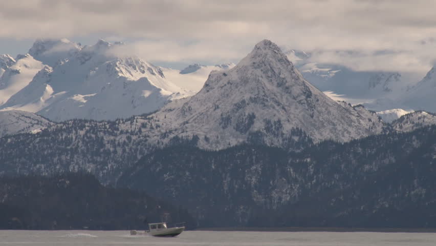 A small fishing/power boat zooms out the bay with snow-gilded mountains beyond.