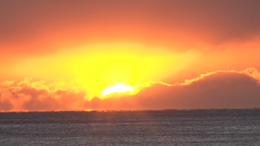 Intense glowing orb sunset over shimmering waves way offshore in heavy clouds.
