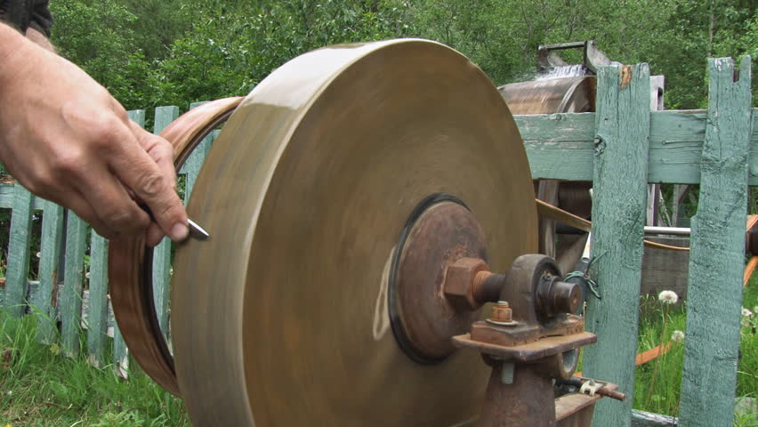 Close up of man sharpening knife at waterwheel-driven grindstone.