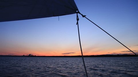 View from the deck of a sailboat, rigging and foresail silhouetted against a brilliant sunset sky