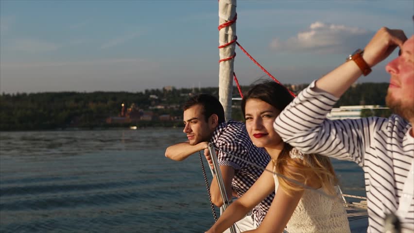 Friends enjoying quiet water travel by yacht. They sailing along the river at sunset and looking at nature scenes