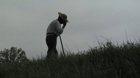 VIRGINIA - 2017. Re-enactment recreation of 1700-1800s Southern American Slavery, slave era. Enslaved African-American. Working in field, laboring in bondage with tool. tattered clothing, Field slave.