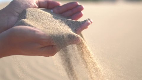 Close up of woman pouring sand running through fingers slow motion at the beach with sun flare