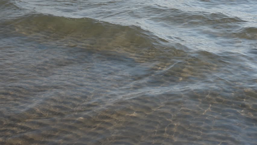 Tracking slow motion sunlit lake wave in shallow water. Rippled sand pattern below. Lake Ontario. Summer at North Beach Provincial Park, Prince Edward County, Ontario, Canada.

