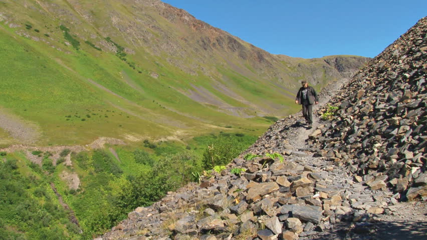 Some guy walks quickly down a rocky alpine trail.