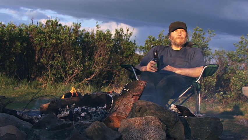 A long golden evening in Alaska - a man relaxes in a camp chair by an open fire,