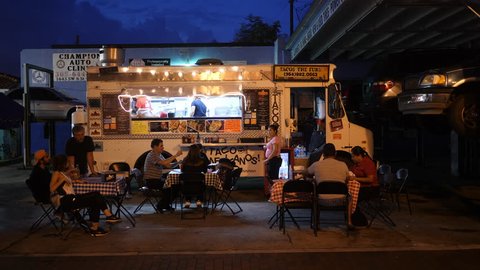 Miami, August 2017. Taco truck on sidewalk with people eating at little tables in Cuban neighborhood Little Havana. Night time.