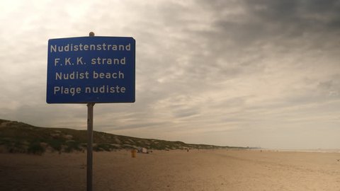 Sign 'Nudist Beach' at sandy beach in Holland. International sign in English, Dutch and French.