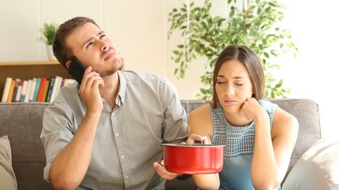 Upset couple calling insurance for home leaks sitting in a couch in the living room in a house interior