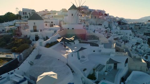 Flying above white houses and famous old castle ruins on Santorini Island, Greece. Village of Oia. Morning sunshine rays.