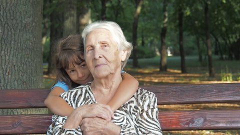 A child is hugging an elderly woman. Little girl with her grandmother in the park.