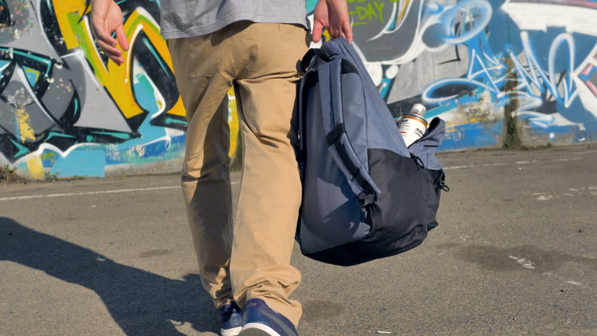 An open backpack with paint cans hangs from a male hand. 
