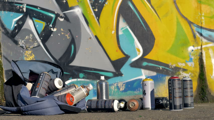 Spray paint cans fallen from a backpack on a pavement. 