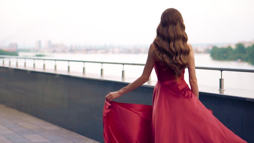 Beautiful woman in red fluttering dress. Urban background. Slow motion.