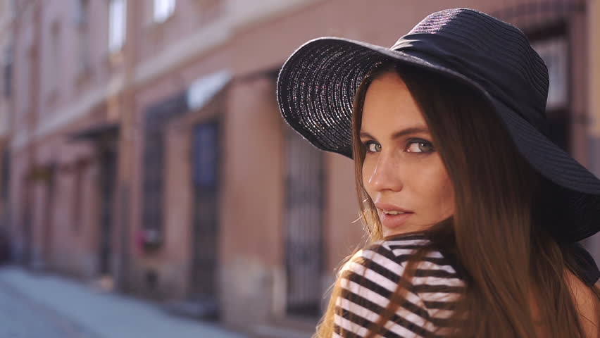 Stunning brunette with long hair poses in black hat on the evening street