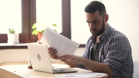 Stressed unmotivated man confused by mistake in documents, looking through papers, frowning using laptop, failing urgent task, missing deadline, quits after bad work fed up with difficult job