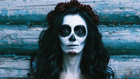 The Mexican Day of the Dead. The portrait of young woman with frightening make-up for Halloween on the background of wooden wall. 4K
