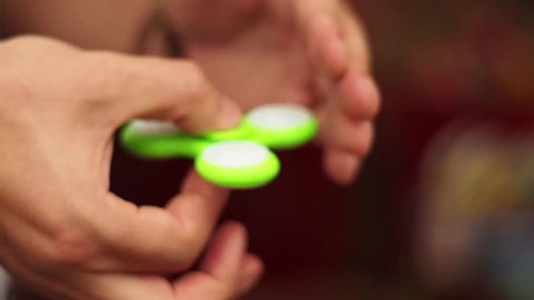 Green hand spinner in hands. Man playing with a fidget spinner, a popular toy which helps to overcome stress and increase concentration. Relaxation and antistress effect. Close up. 