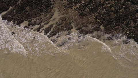 Floating top down aerial track of shoreline and low tide textured landscape at Seaford near Beachy Head in the UK