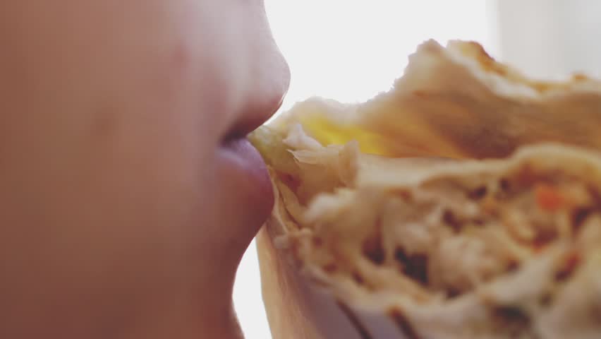 Young woman is eating doner kebab at lunch bites a delicious juicy shawarma. Fast food concept. Mouth close up in slow motion. 1920x1080