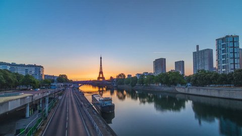 Eiffel Tower sunrise timelapse with boats on Seine river and in Paris, France. View from Grenelle bridge. Modern buildings and traffic on a road