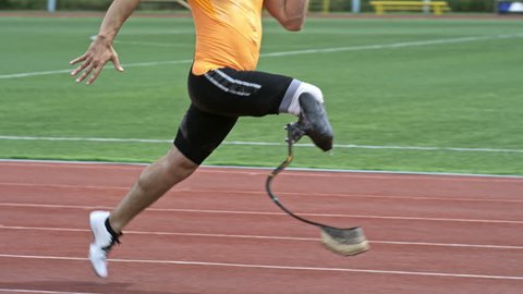 Slow mo side view of amputee athlete with prosthetic blade running on stadium track outdoors