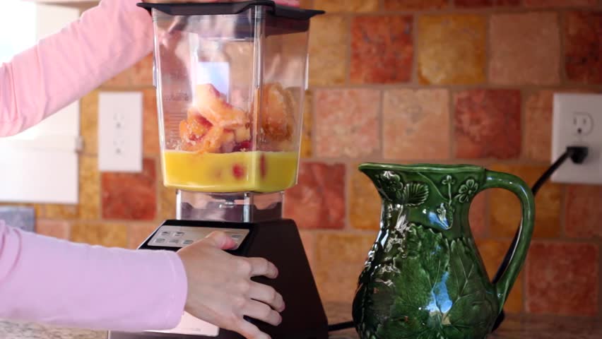 A woman makes a fruit smoothie in a blender