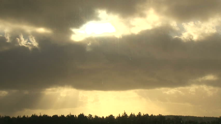 Sunlight shining through heavy rain cloud over trees at sunrise, time lapse.
