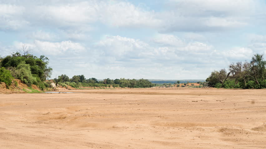 A long day-time timelapse of a dry riverbed  at the start of summer with dramatic stormy clouds. 4K