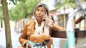 Senior woman in town with bike, talking on phone
