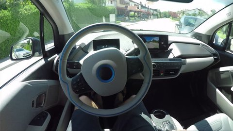 CLOSE UP, POV: Man in futuristic automated electric car. Vehicle parallel parking by itself in suburban town street. Self-steering automatic computer vision auto turning wheel and parking on spot