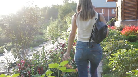 A woman walks along the path among the flowers. woman walking in the stone garden. woman with a female backpack walks in the park.