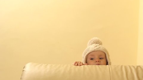 Cute baby head with big fez showing up behind the couch while standing up and practicing first steps