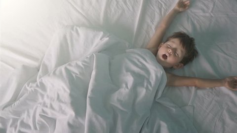 Little boy stretching in bed after wake up