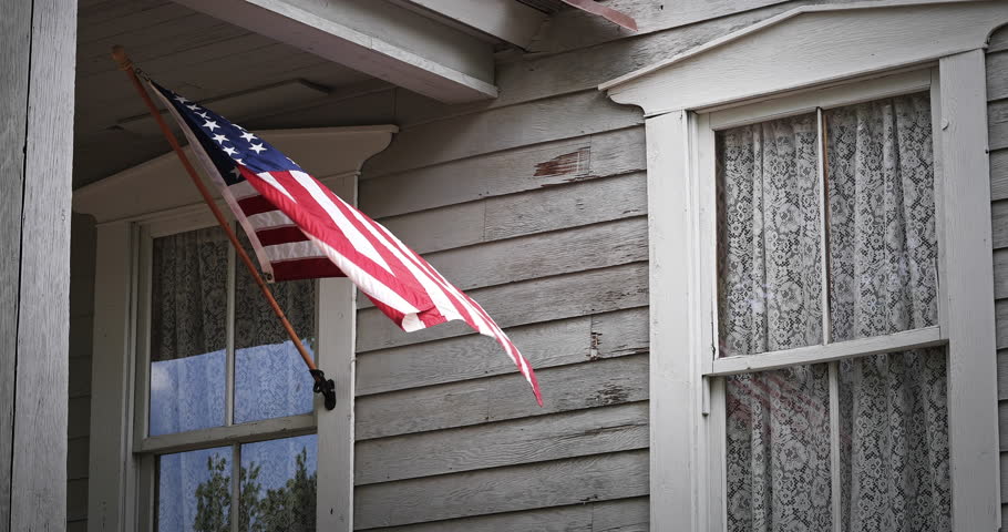 An American flag gently waves on a Victorian house front porch. Royalty-Free Stock Footage #31341520