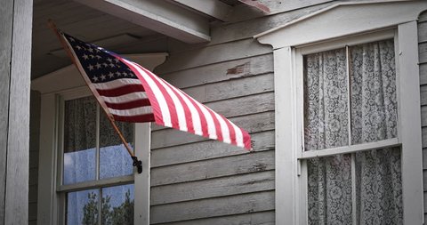 An American flag gently waves on a Victorian house front porch.