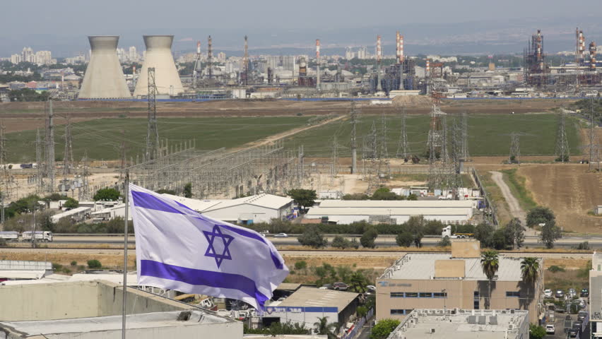 A flag of Israel hanging in sunny and windy day with Industrial district near Haifa on the background