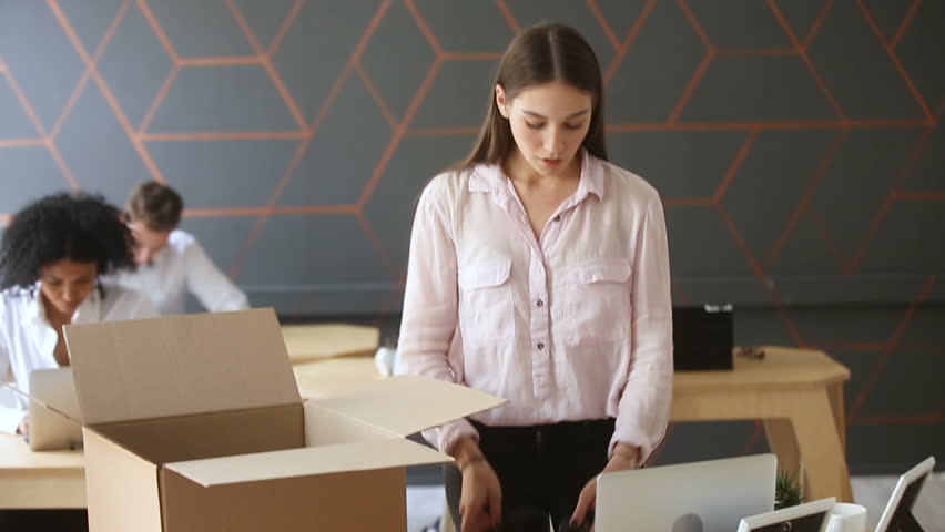Fired young sad woman packing box standing near work desk, taking all her belongings after being dismissed resignation, upset employee quits from job collecting personal stuff at workplace to leave Royalty-Free Stock Footage #31351963