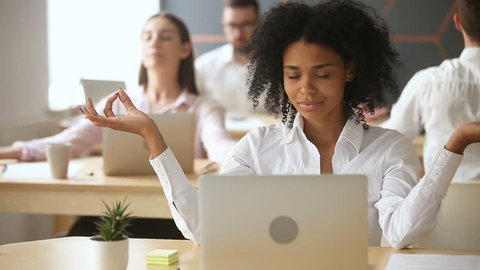 African businesswoman meditating with multiracial colleagues in office, businesspeople doing group yoga exercises indoors at workplace, corporate meditation, keeping mental balance at stressful job