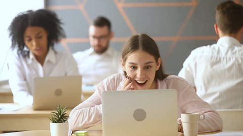 Young excited employee looking at laptop screen with surprise, gossip girl sharing good funny news with coworkers, spreading rumors in coworking office, colleagues talking at workplace, word of mouth