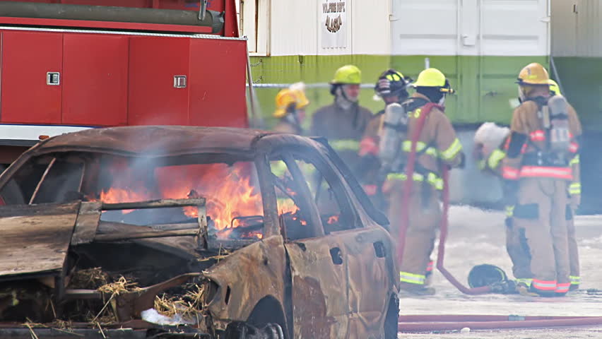 HOMER, AK - CIRCA 2012: A car burns in the foreground while firefighters prepare