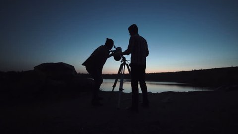 Silhouettes of people looking through telescope on shore of lake in dark. Stock Video
