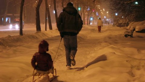 Father Pulling Son On Sledge Along Snowy Street.A dad pulling on the snow his son sitting on the sledge.HD1080p.