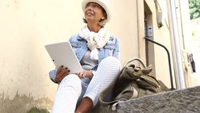 Senior woman sitting in town using digital tablet