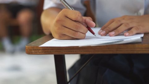 Closeup to hand of student  holding pen and taking exam in classroom with stress for education test