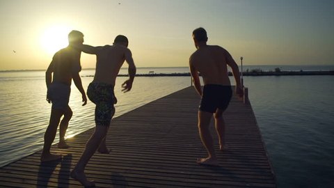 Group of friends running and jumping off sea pier in the water rapid slow motion