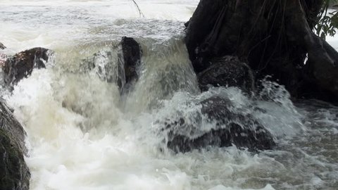Raging clean fresh mountain river flowing between rocks in slow motion. Taken outdoor on cloudy day.