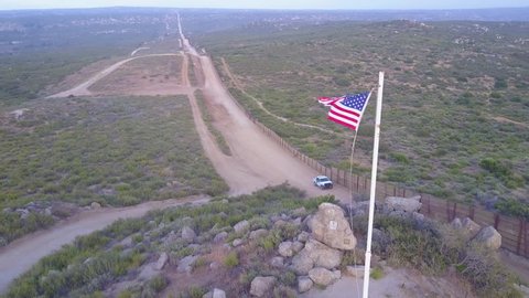 CIRCA 2010s - U.S.-Mexico border - The American flag flies over the U.S. Mexico border wall in the California desert as a border patrol passes beneath.